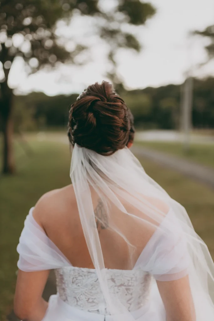Eleganckie, niskie upięcie ślubne z ozdobną biżuteryjną spinką i wpiętym welonem