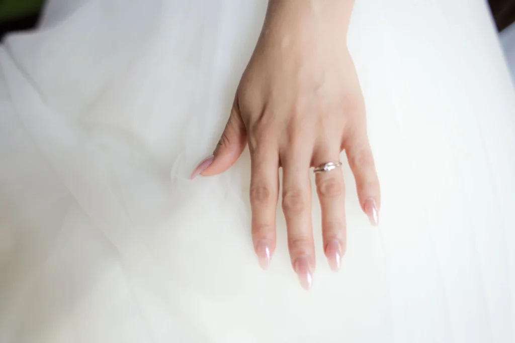 Subtelny manicure ślubny baby boomer na paznokciach w kształcie migdała z widoczną obrączką